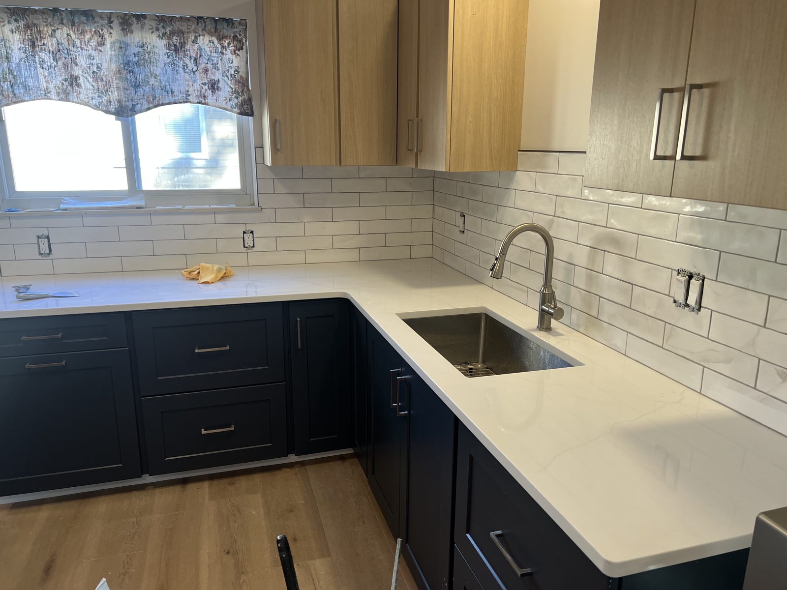 White handmade-look subway tile backsplash wrapping an L-shaped kitchen corner between white quartz counters and white oak upper cabinets